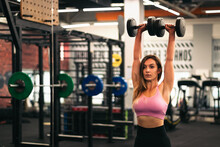 Woman Athlete Training With Dumbbells In Front Of The Mirror In A Gym