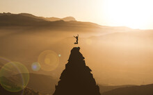 Young Woman Jumping On Top Of Mountain Peak Celebrating Success. Businesswoman Climber Success And Goal Achievement Concept. Cliff Climbing Adventure. Sunset Mountains, Female Silhouette