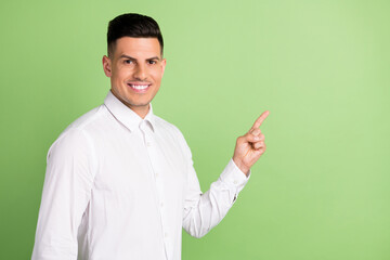 Photo of sweet charming young gentleman wear white shirt smiling pointing finger empty space isolated green color background