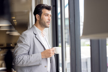 Businessman with cup of coffee looking out of window at office