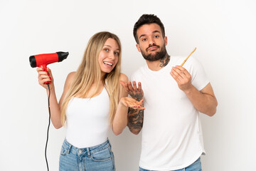 Wall Mural - Couple holding a hairdryer and brushing teeth over isolated white background having doubts while raising hands and shoulders