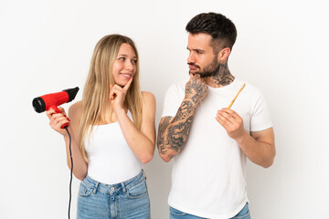 Poster - Couple holding a hairdryer and brushing teeth over isolated white background looking looking at each other