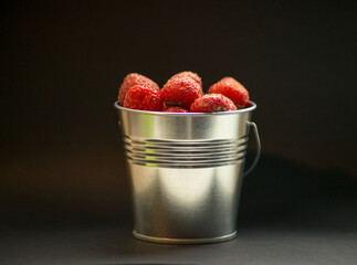 Fresh red strawberries in metallic bucket on black background close-up. Tasty Red summer berries.