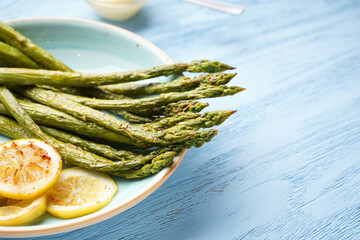 Baked asparagus with lemon on wooden background, place for text. Close-up.