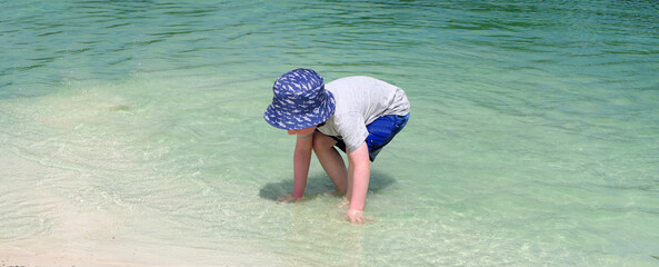 Small boy with a blue sun hat playing on a fresh water sandy beach in Vacation resort in Ireland