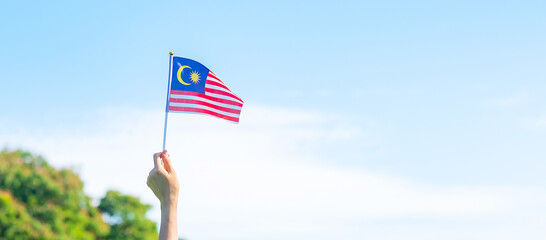 hand holding Malaysia flag on blue sky background. September Malaysia national day and August Independence day