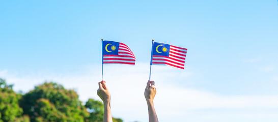 Wall Mural - hand holding Malaysia flag on blue sky background. September Malaysia national day and August Independence day