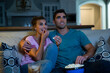 © SuperStock - Young couple sitting on couch watching a movie at home with a bowl of popcorn