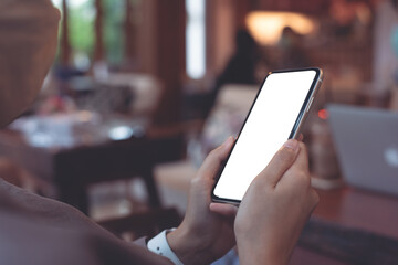 Wall Mural - Cell phone mockup image blank white screen.  Woman hand holding, using mobile phone in coffee shop, close up