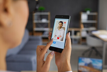 Finding love online using dating websites or mobile apps: Woman who's looking at profile pics with red hearts and message buttons on phone display gives a like to handsome young man. Closeup, close up