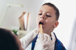 © Mediteraneo - Doctor checking little boy's throat in the office