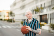 Young and thoughtful albino blond man, with basketball ball and headphones, walking in the city