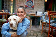 A young beautiful girl is posing for a photo in the bar in a hug with her dog. Leisure, bar, friendship, outdoor