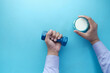 young man hand holding dumbbell and glass of milk on blue 