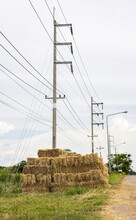 Many Bales Of Straw Were Piled On The Side Of The Road Near The Electric Poles.