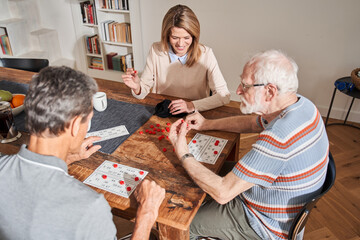 Wall Mural - People sitting at the table in front of their caregiver while playing at the bingo game