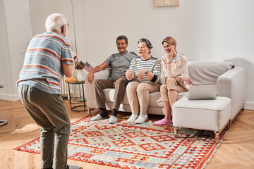 Wall Mural - Senior man standing in front of the pensioners and caregiver and showing something