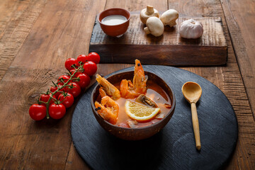 Tom yam soup with shrimps and coconut milk on the table on a round board near milk and a wooden spoon.