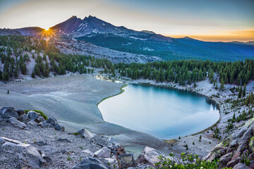 Wall Mural - sunrise over clear blue alpine lake surrounded by fir trees and volcanic mountain peaks.