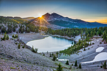 Wall Mural - sunrise over clear blue alpine lake surrounded by fir trees and volcanic mountain peaks.