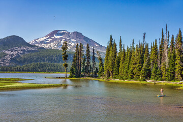 Wall Mural - a lone stand up paddle boarder crosses a mountain lake surrounded by fir trees and volcanic mountain