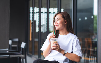 Canvas Print - Portrait image of a beautiful young asian woman holding and drinking iced coffee in cafe