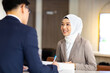 © NVB Stocker - Portrait of muslim woman receptionist at desk in lobby.  Asian business man standing at reception desk and talking to muslim woman receptionist.