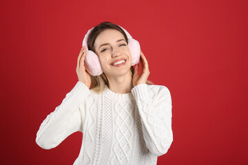 Canvas Print - Happy woman wearing warm earmuffs on red background