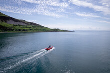 A Red Passenger Ferry Motors Alongside A Beautiful Coastline