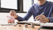 © Puwasit Inyavileart - Man puts a coin dollar in a piggy bank, Saving money for future growth and knowing how to manage your spending wisely, Saving money for business growth or long-term profitability.