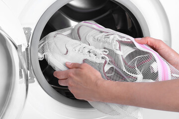 Poster - Woman putting pair of sport shoes in mesh laundry bag into washing machine, closeup