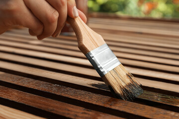 Wall Mural - Woman applying wood stain onto planks outdoors, closeup