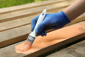 Woman painting wooden surface with coral dye outdoors, closeup