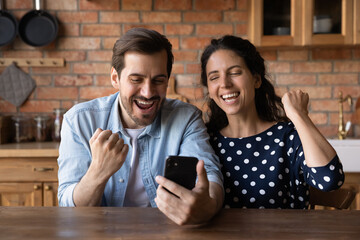 Wall Mural - Excited millennial couple with smartphone celebrating success, approver loan, mortgage, getting good news, winning prize. Happy husband and wife using mobile phone, making winner yes gesture