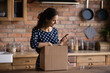 © fizkes - Happy shopper receiving purchase from internet shop, using app on mobile phone for giving positive review to store. Woman packing parcel for sending, using smartphone, ordering delivery service