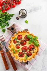 Wall Mural - Homemade quiche tart with cherry tomatoes, basil, seasonings and cheese on white stone background. Selective focus