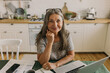 © shurkin_son - Smiling middle-aged female sitting at home workplace with laptop and documents. Cheerful elderly female looking at camera with happiness. Distance working and remote work concept