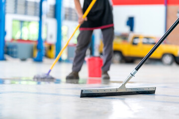 Wall Mural - Select the focus mop, service staff man using a mop to remove water in the uniform cleaning the protective clothing of the new epoxy floor in an empty warehouse or car service center.