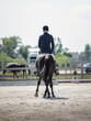 portrait of man rider and black stallion eventing horse trotting leg-yield during equestrian dressage competition in summer