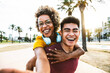 © Davide Angelini - Multiracial couple taking selfie portrait with smartphone mobile outdoor - Asian guy giving a piggyback ride to hispanic girl on city street - Tourism, friendship, youth and weekend activities concept
