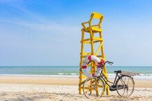 Old Retro Black Bicycle With Flowers Bouquet Beside Life Ring For Life Safety On Yellow Lifeguard Stand Station Or Lifeguard Chair Protecting The Safety Of Tourist On The Empty Beach In Sunshine.