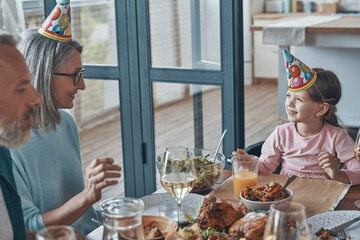 Happy family celebrating birthday of little girl while sitting at the dining table at home