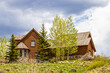 Luxury log cabin with wooden roof and rock bay window on hilltop surrounded by pines and quaking aspens