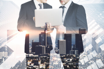 Poster - Attractive young european businessmen using laptop together on abstract bright city background. Success, teamwork and communication concept. Double exposure.