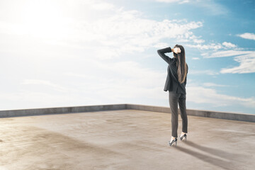 Wall Mural - Thoughtful young businesswoman standing on building roof on beautiful sky background with mock up place for your advertisement. Success and future concept.