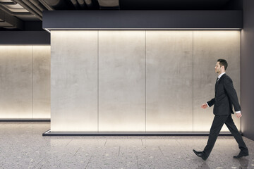 Poster - Businessman walking in modern exhibition space concrete interior with mockup place on wall. Mock up.