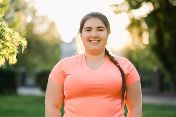 Happy woman. Body positive. High self-esteem. Good attitude. Cheerful young obese overweight lady smiling outside in defocused summer park street landscape.