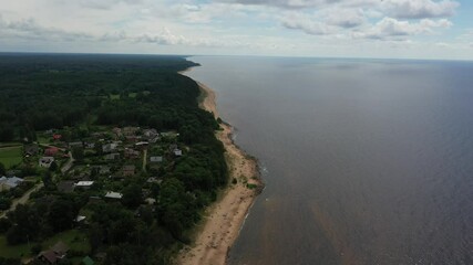 Sticker - An aerial view of a sea and dense green forest with residential buildings under a cloudy sky in 4K