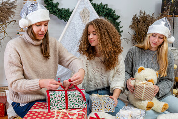 young girls having fun wrapping gifts at home, great teamwork of friends packing presents for christmas