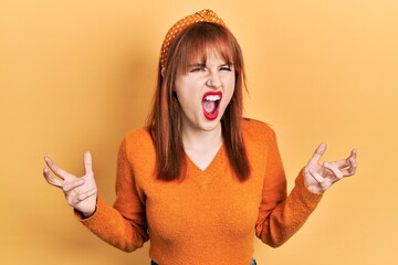 Poster - Redhead young woman wearing casual orange sweater crazy and mad shouting and yelling with aggressive expression and arms raised. frustration concept.